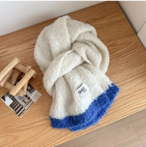 Detail of soft beige knit scarf with blue contrast and GQD label on wooden desk