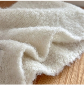 Close-up of soft white wool blend knit texture with fluffy fibers on a wooden surface