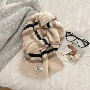 Striped wool blend knit scarf in beige with black stripes on a cozy white bed