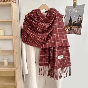 Detail of burgundy plaid scarf with fringe edge and small woven tag on white coat