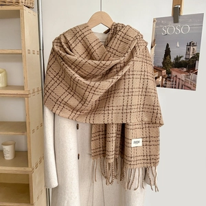 Detail of classic plaid scarf with thick texture and long decorative fringes on wood hanger