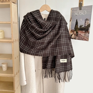 Detail of dark brown plaid scarf with thick knit texture and fringe on white coat