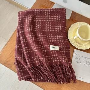 Close-up of burgundy plaid scarf with fringe and brand label on a cozy wooden desk