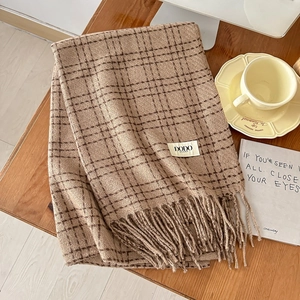 Close-up of thick plaid scarf texture with soft tassels on a wooden table with coffee