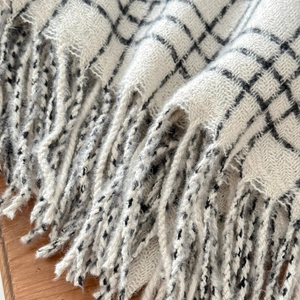 Detail of warm white plaid scarf featuring thick tassels and soft knit texture
