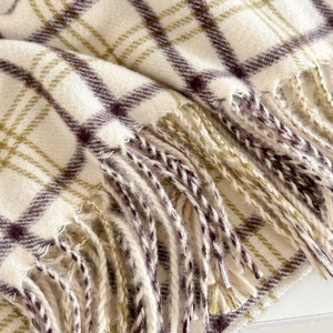 Close-up of beige plaid scarf fabric with purple stripes and soft woven fringe details