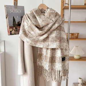 Detail of plaid cashmere-like scarf with dense tassels hanging on a wooden hanger