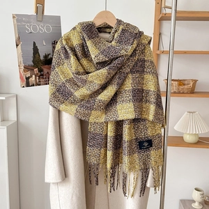 Detail of plaid cashmere-like scarf with tassels styled on a coat in a home setting