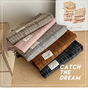 Detail of multi-color plaid scarves with fringe and brand label on a wooden surface