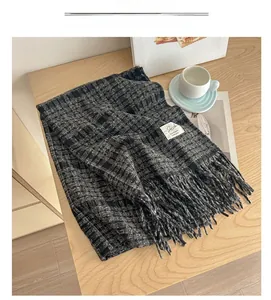 Detail of plaid scarf with fringe and woven label on a minimalist wooden background