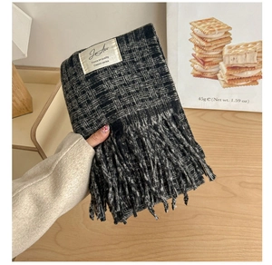 Detail of soft knit texture and fringe on a black and grey plaid scarf