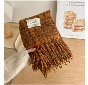 Detail of brown and black plaid scarf with long fringe and woven texture on a wooden desk
