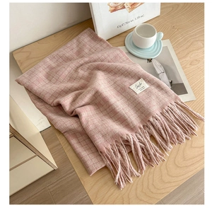 Detailed view of pink plaid knit scarf with fringes and minimalist label on wooden table
