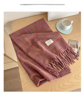 Detail of pink and brown plaid scarf with fringe and white woven label on wood desk