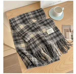 Close-up of black and grey checkered knit scarf with tassels on a wooden table