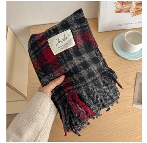 Close-up of red and black plaid scarf texture with tassel detail and white fabric label