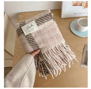 Detailed view of beige plaid scarf with soft tassels and woven brand label on wood table