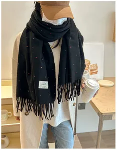 Close-up of black knit scarf with colorful polka dots, soft fringe, and side woven label