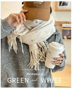 Detail of cream knit scarf with colorful specks and fringe on a model with coffee