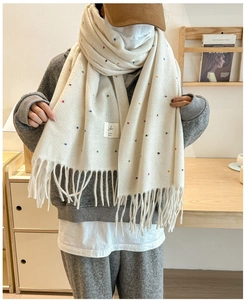 Detail of cream knit scarf with colorful dots and long tassels on a wooden background