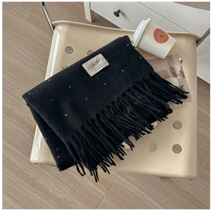 Close-up of black knit scarf with colorful polka dot embroidery and dense tassel fringe