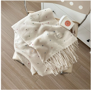 Close-up of cream knit scarf featuring colorful dot patterns and elegant tassel fringe