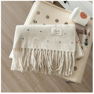 Macro detail of cream knit scarf featuring colorful specks and long tassel edges