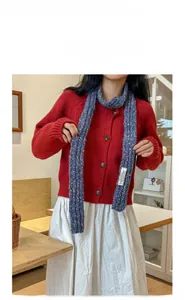 Detail of blue speckled knit scarf paired with red cardigan and white skirt