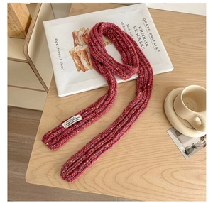 Detail view of pink speckled knit scarf with a woven label on a wooden table