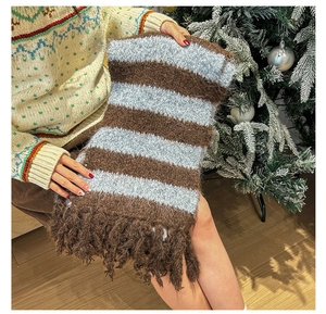 Detailed knit texture of soft striped scarf with fringe, shown in cozy winter setting