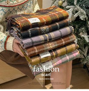 Stacked colorful plaid scarves with soft fringes and woven brand label in a warm cozy setting