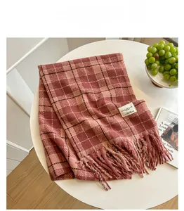 Detail of red and pink plaid scarf with fringe and label on a white tabletop setting