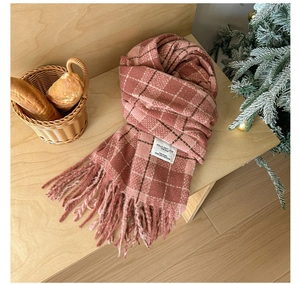 Close-up of pink plaid knit scarf with fringes and authentic woven label on wood