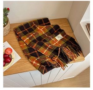 Detail of plaid scarf with orange and brown checkers and long tassels on wood