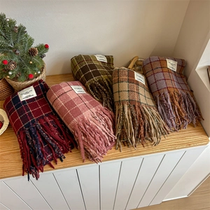 Winter plaid tassel scarves in multiple colors neatly stacked on a wooden table surface