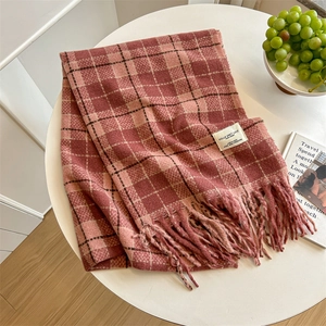 Cozy pink plaid scarf with tassels and fabric label on a white table setting
