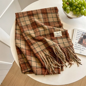 Retro plaid cashmere-feel scarf with tassels and brand label on a minimalist white desk