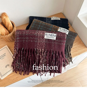 Three plaid tassel scarves in burgundy, brown and blue on a cozy winter wooden setting