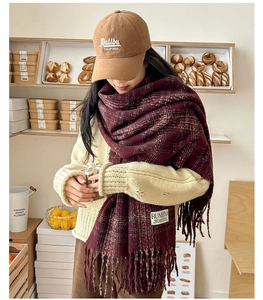 Detail of burgundy plaid scarf with soft fringe and logo tag for winter warmth