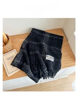 Detailed view of soft plaid scarf texture with long fringe and woven label on wood table