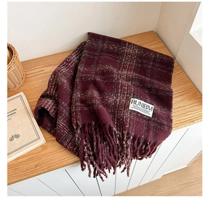 Close-up of vintage burgundy plaid scarf with tassels and brand label on wooden surface