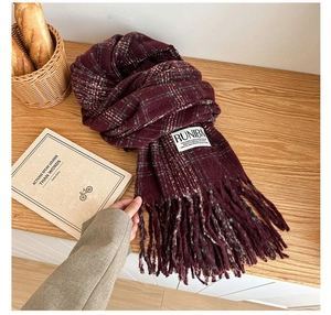 Detailed shot of a burgundy plaid scarf with tassels and fabric label on a wood table