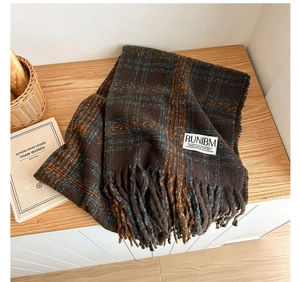 Detail shot of thick plaid scarf with long tassels and woven label on a wooden surface