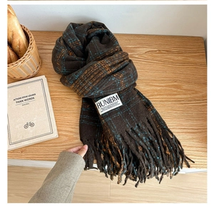Close-up of brown plaid scarf with long tassels and fabric label on wooden table
