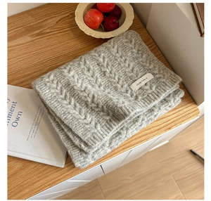 Detail of grey cable-knit scarf with woven label on a rustic wooden table setting