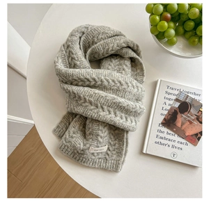 Detail of grey cable knit wool scarf with a vegetable fabric label on a white table