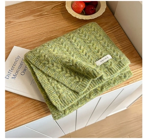 Close-up of grass green chunky knit scarf with twist texture on wood table