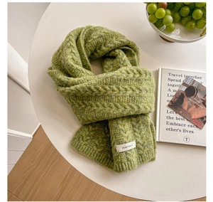 Detailed macro view of moss green chunky knit scarf featuring cable patterns and white label