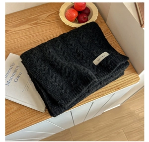 Detail of black thick cable knit scarf texture with a woven label on a wooden desk