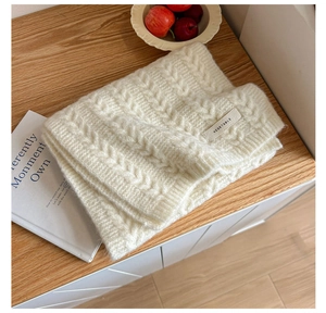 Detail of a white cable knit scarf with a woven Vegetable brand tag on a wooden table